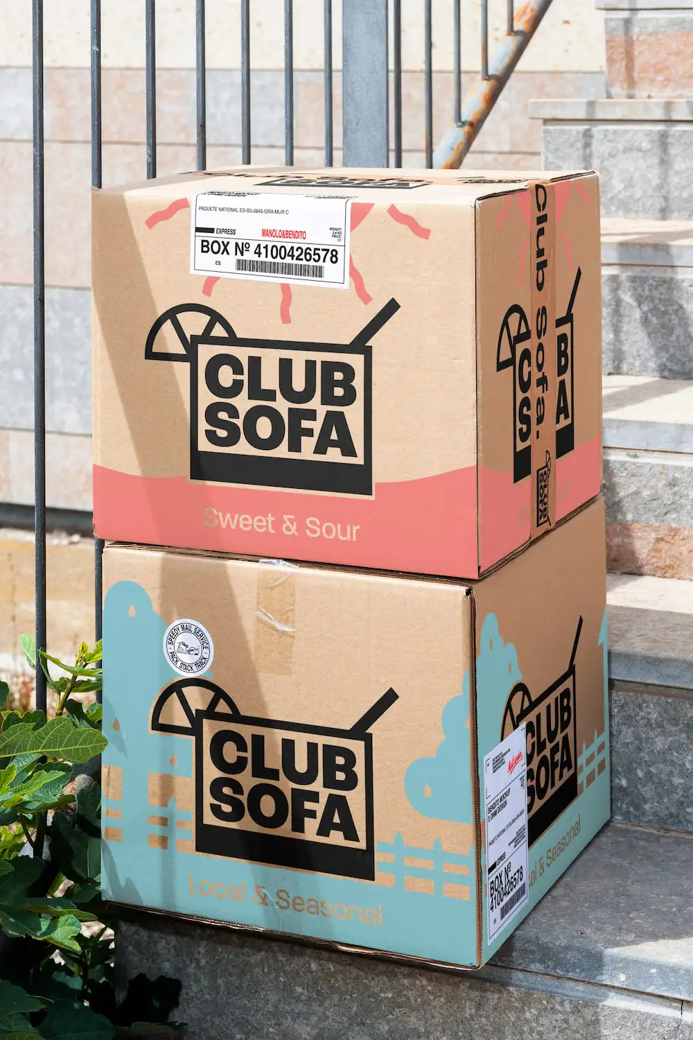 Een afbeelding van twee gestapelde dozen met Club Sofa-branding. Op een doos staat 'Sweet & Sour' en op de andere 'Local & Seasonal'.